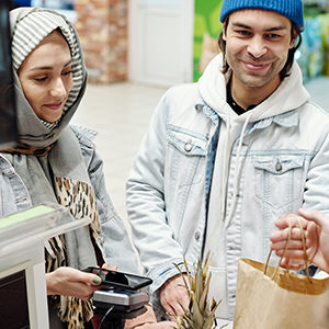 Smiling woman and man purchasing groceries. She is using her phone to pay on the debit machine.