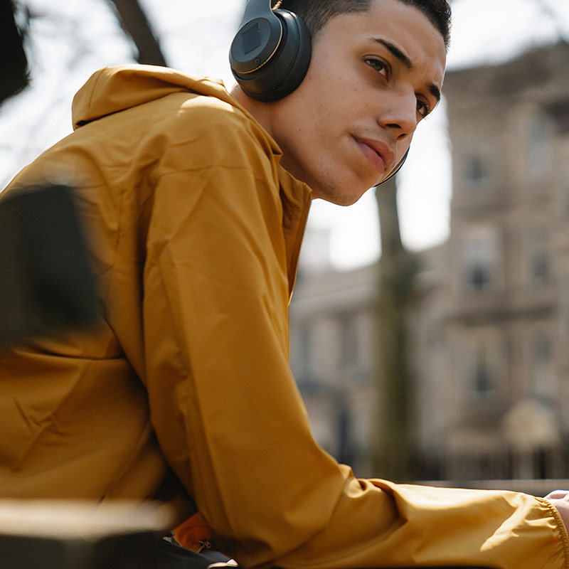 Teen wearing headphones while sitting on a bench and holding phone.