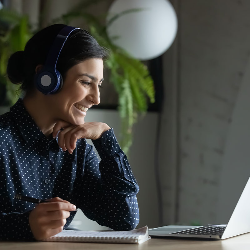 Woman wearing headset looking down at her laptop and smiling.