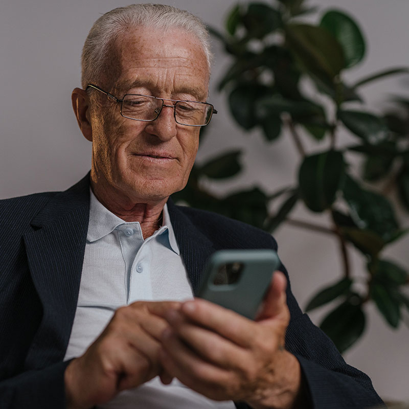 Man with glasses seated on a chair, looking at his phone.